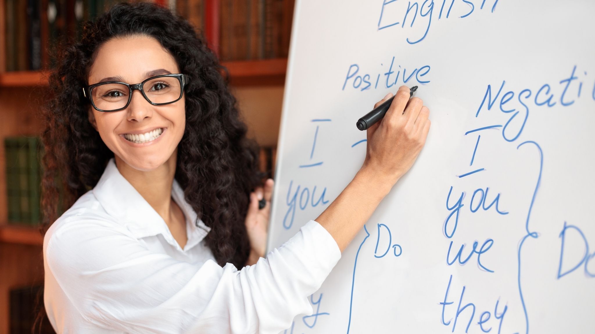 An ESL teacher in a physical classroom writing on the whiteboard