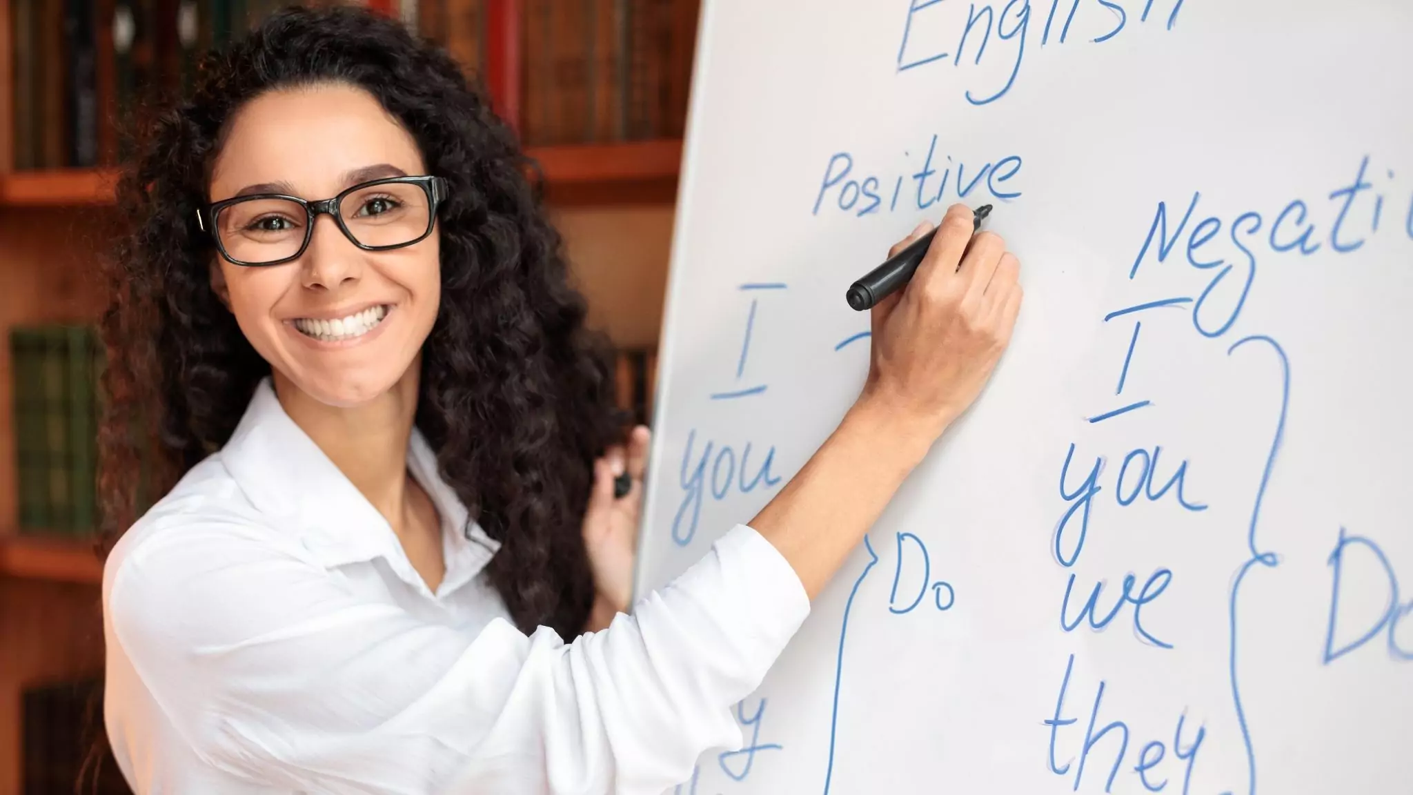 An ESL teacher in a physical classroom writing on the whiteboard
